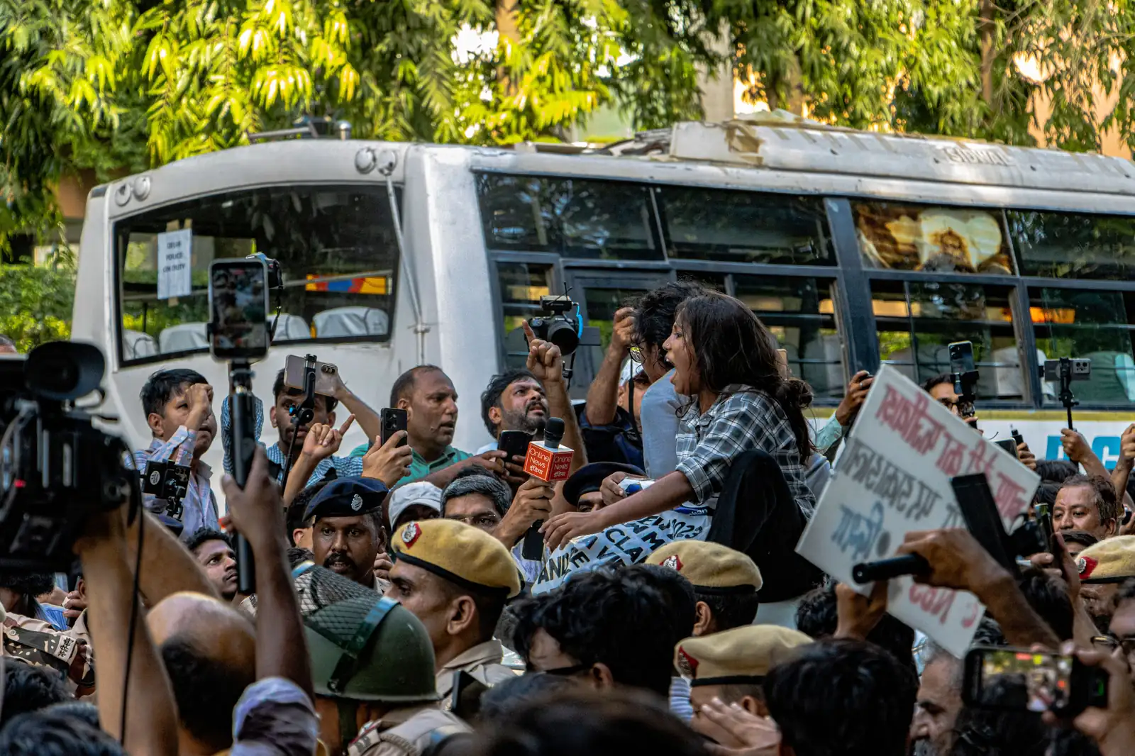 India: Two Trans Women Held Overnight With Male Detainees After Delhi Protest Protesters, police and media crowd around a police bus in Delhi